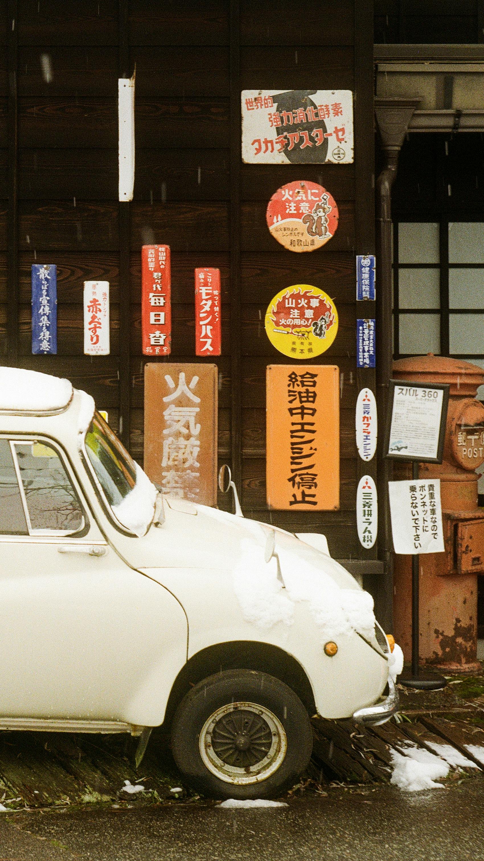Classic car parked by a wall covered in vintage Japanese signs.