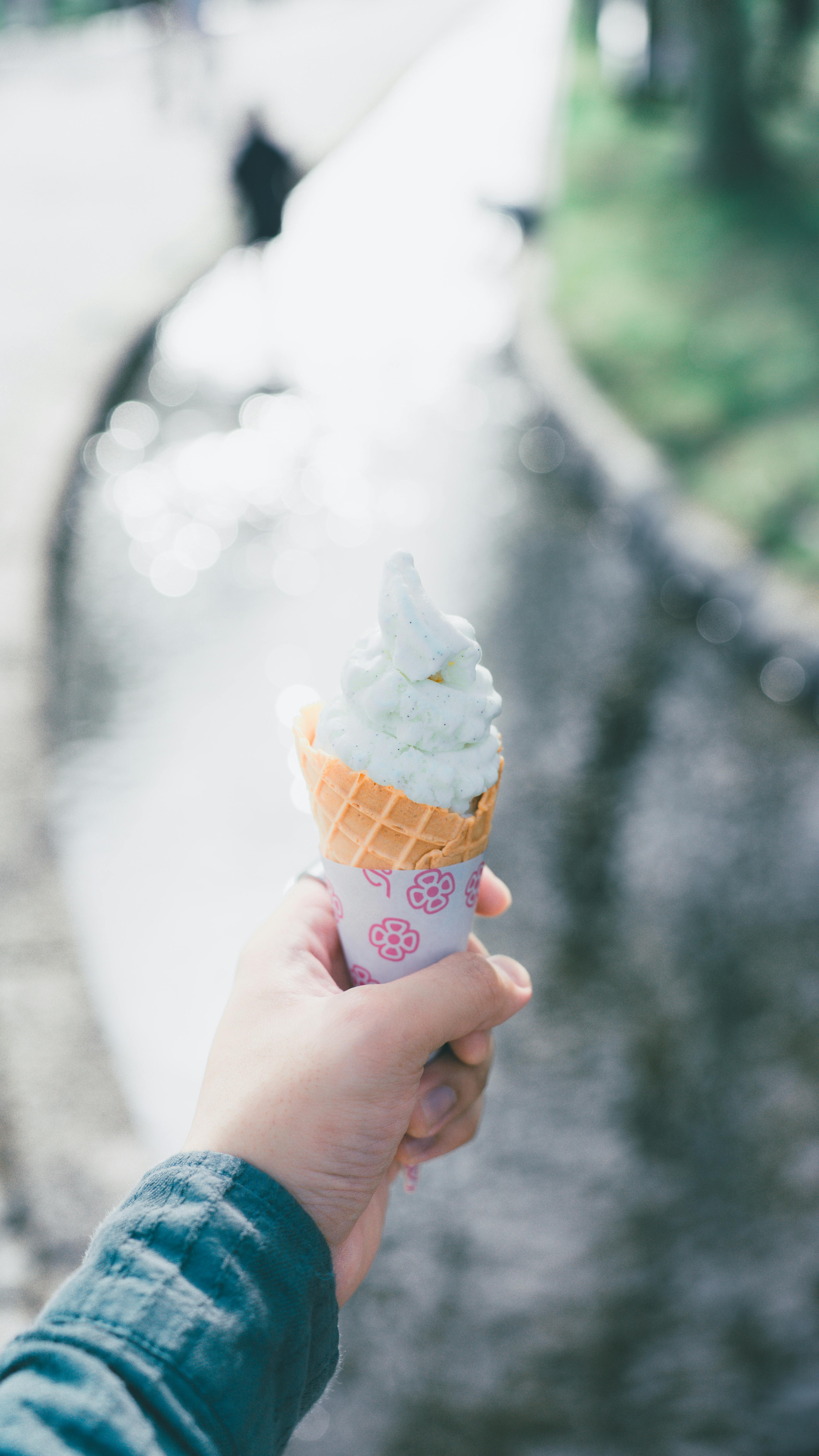 A hand holds an ice cream cone by a flowing stream on a sunny day, evoking a summer vibe.
