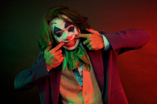 Dramatic male clown with painted face grimacing smile pulling mouth with hands while looking at camera