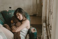 一位沉思的年轻女子抱着泰迪熊，坐在一间饱经风霜的房间里，流露出孤独与沉思