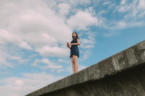Free A fashionable woman stands confidently on concrete edge with a vibrant blue sky above. Stock Photo