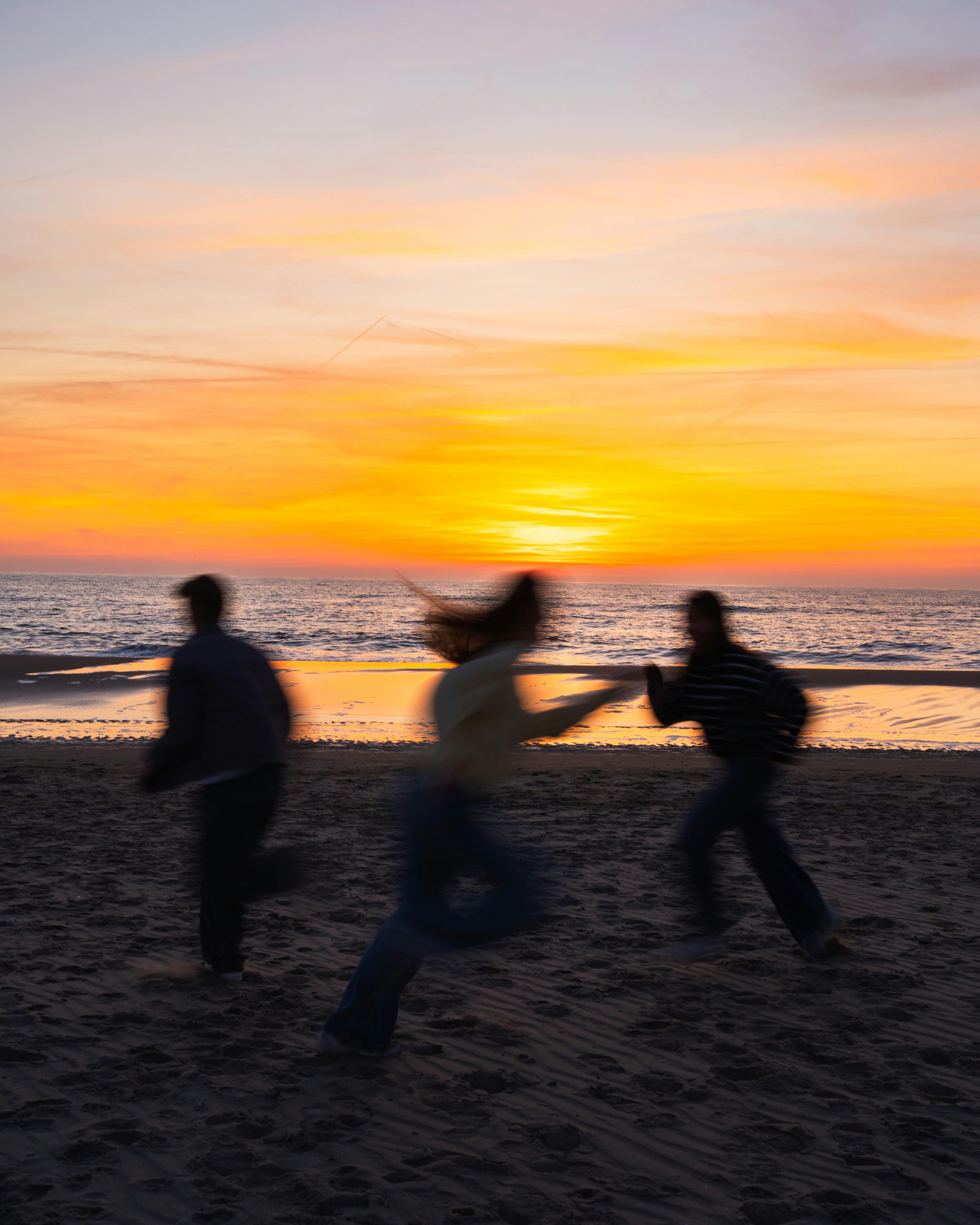 Blurred silhouettes of three people running on a sandy beach during a vibrant sunset.