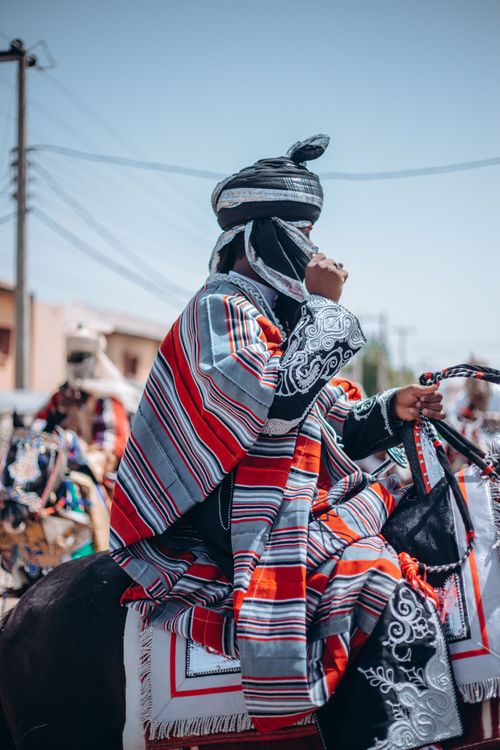 Free A colorful scene of an adult in traditional clothing riding a horse during a cultural parade. Stock Photo