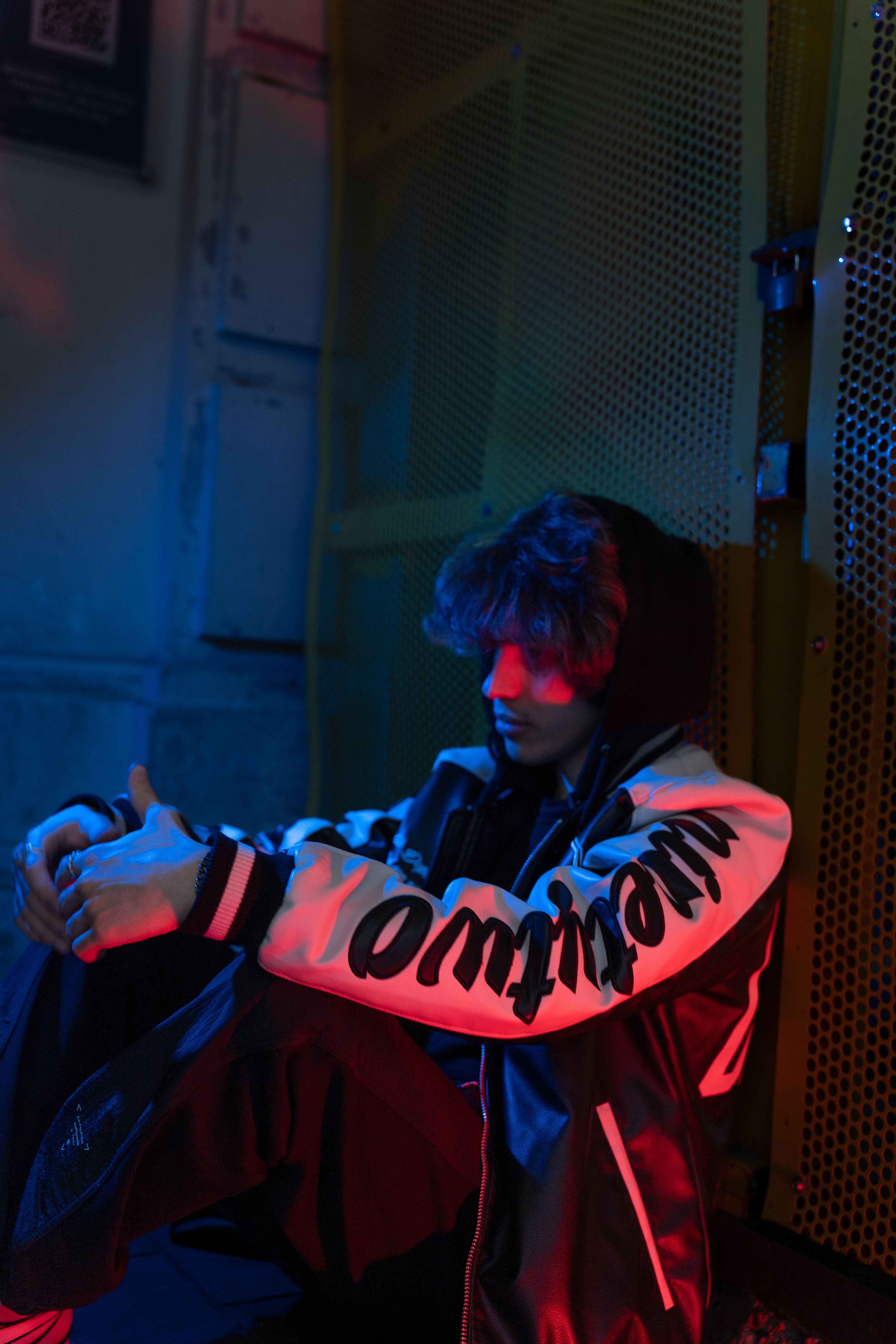 Pensive young adult sitting in urban setting with vibrant lighting.