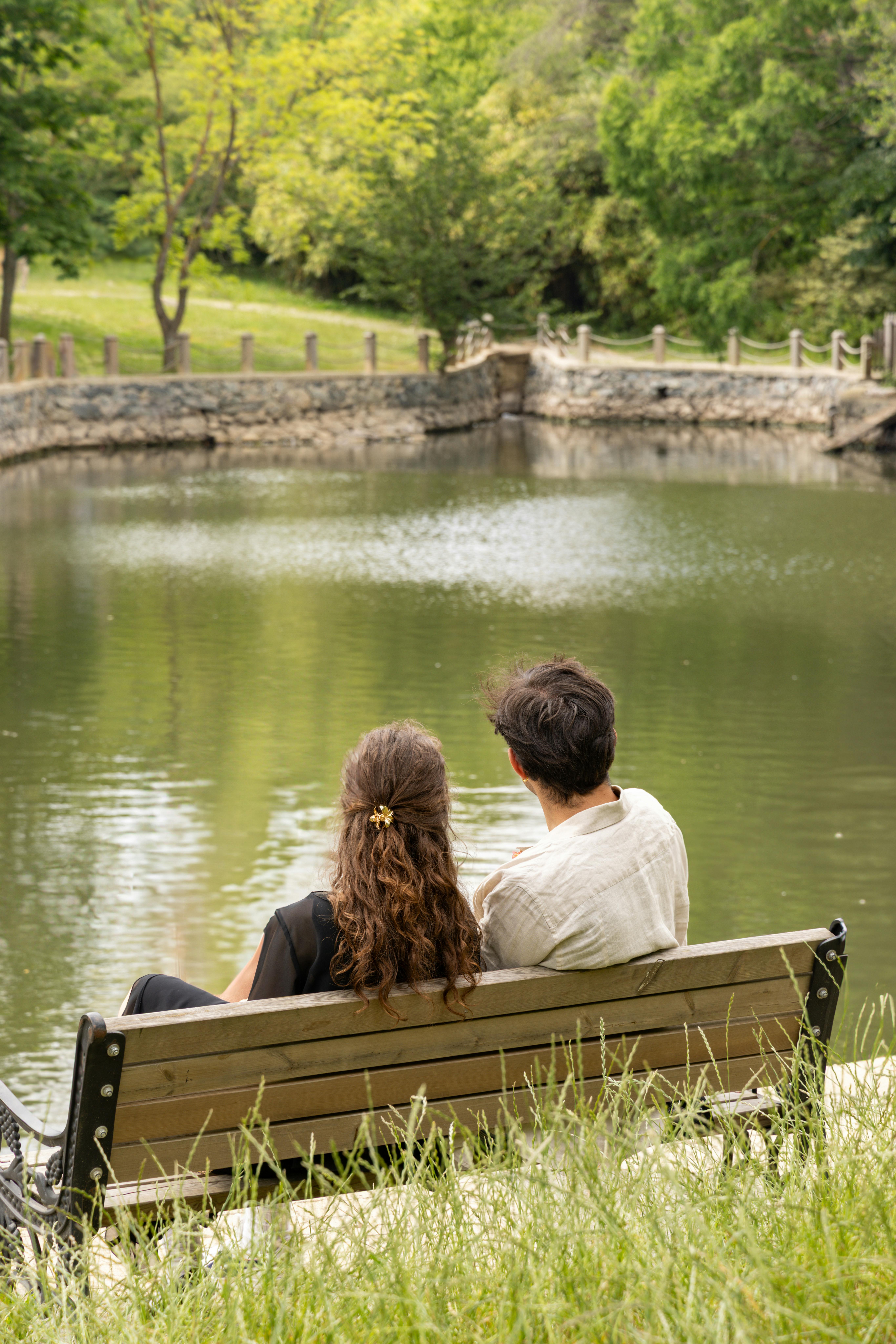 A couple sits on a bench overlooking a tranquil pond in an Istanbul park.