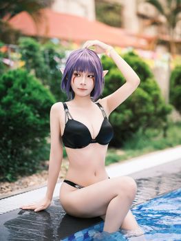 A cosplay model with purple hair posing by a pool in a black bikini outdoors.