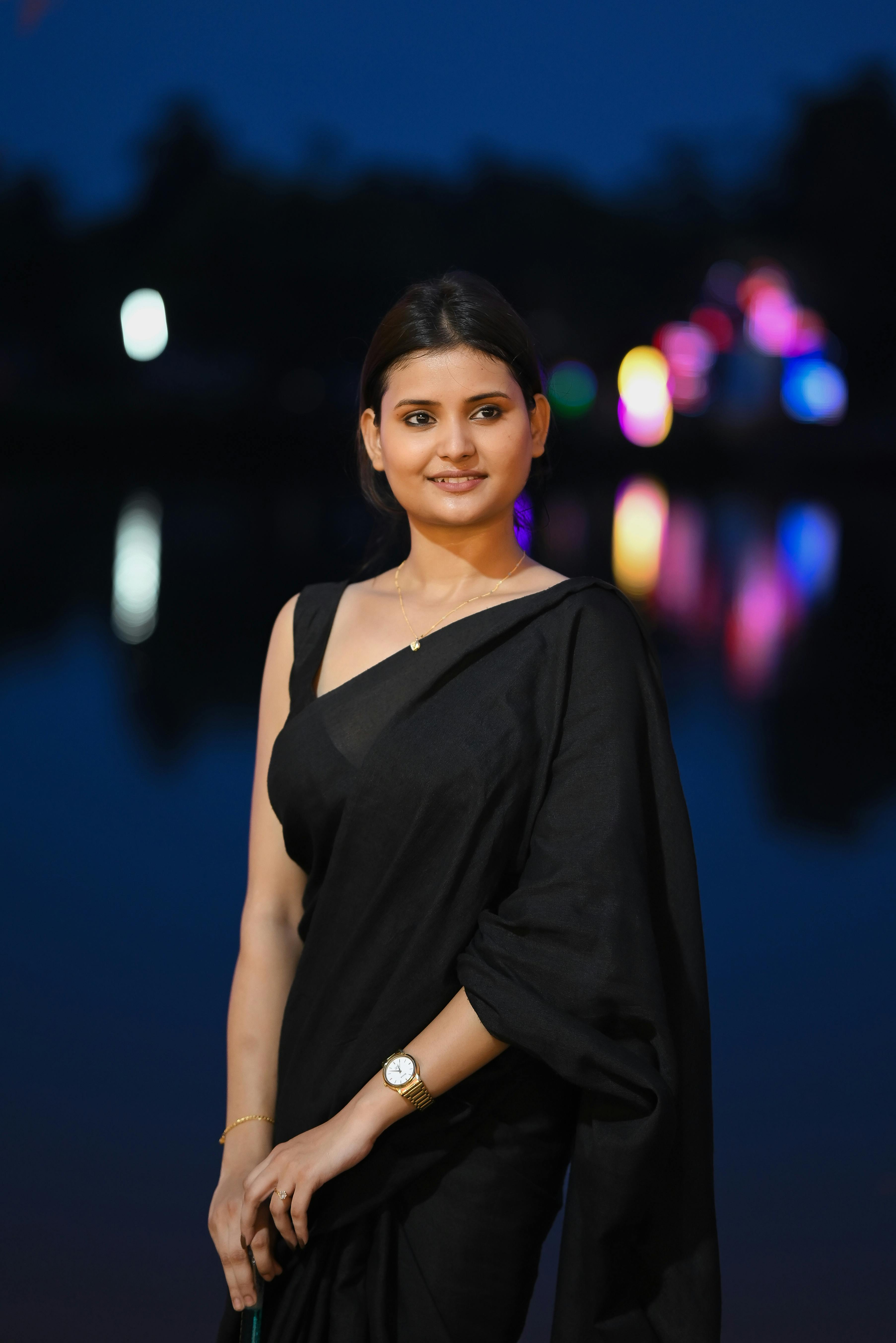A woman in a black saree poses at night, showcasing traditional Indian elegance.
