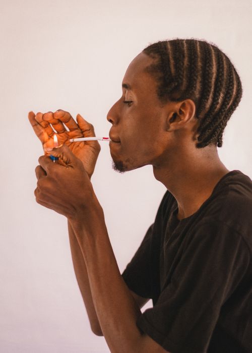 Free A man in a black shirt lights a cigarette against a plain background. Stock Photo