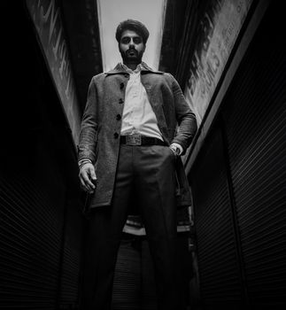 A dramatic black and white portrait of a man in a city alleyway, exuding confidence.