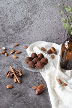 A rustic food presentation with chocolate date truffles, almonds, and cinnamon sticks on a textured surface.