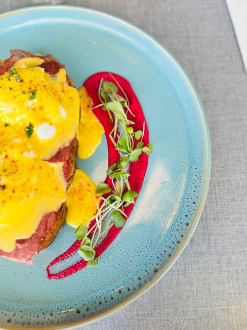 Free Colorful Eggs Benedict with hollandaise sauce on blue plate, garnished beautifully. Stock Photo