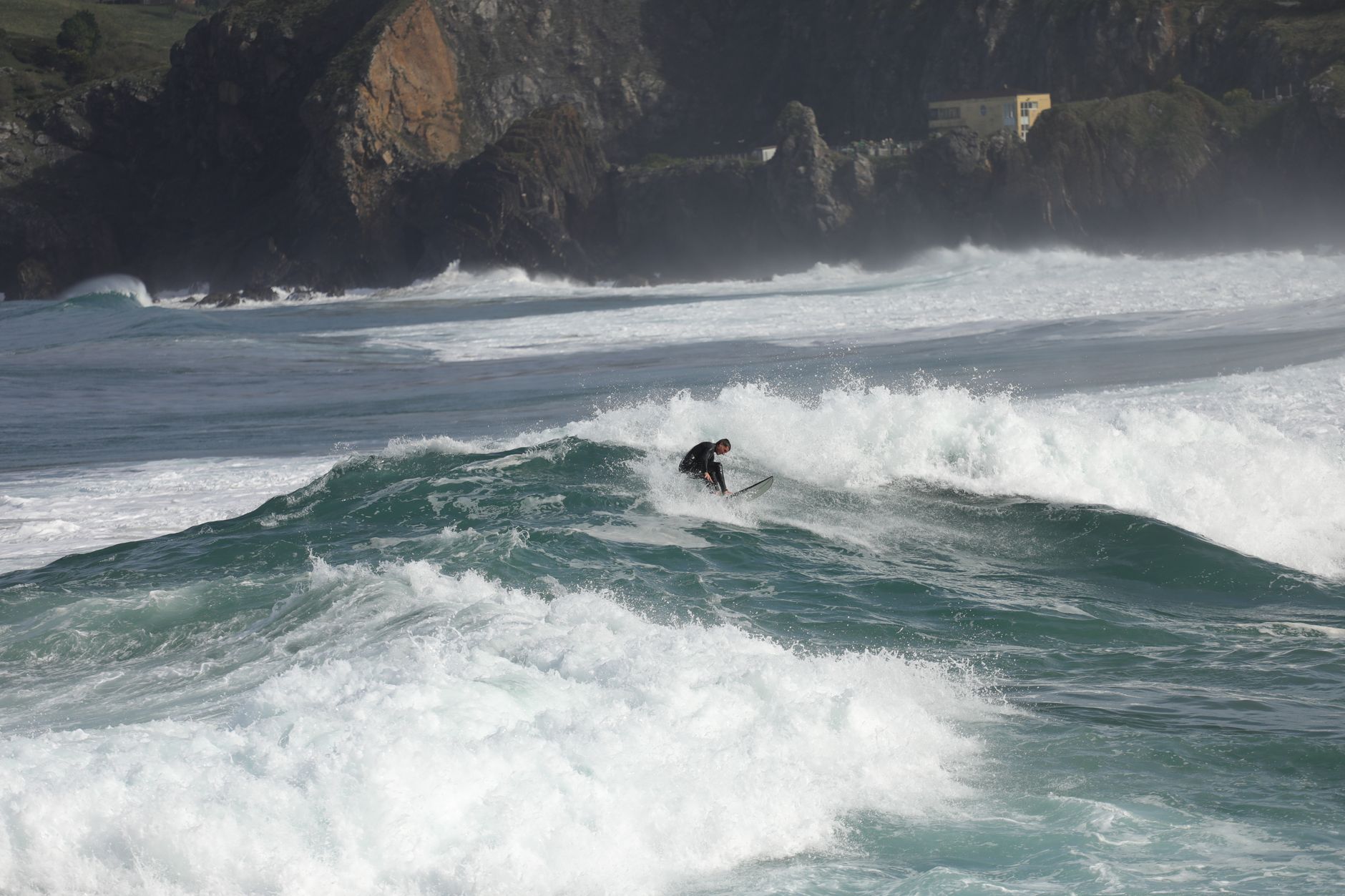 A surfer rides powerful ocean waves on a sunny day in Bakio, Bizkaia, capturing the essence of surf culture.