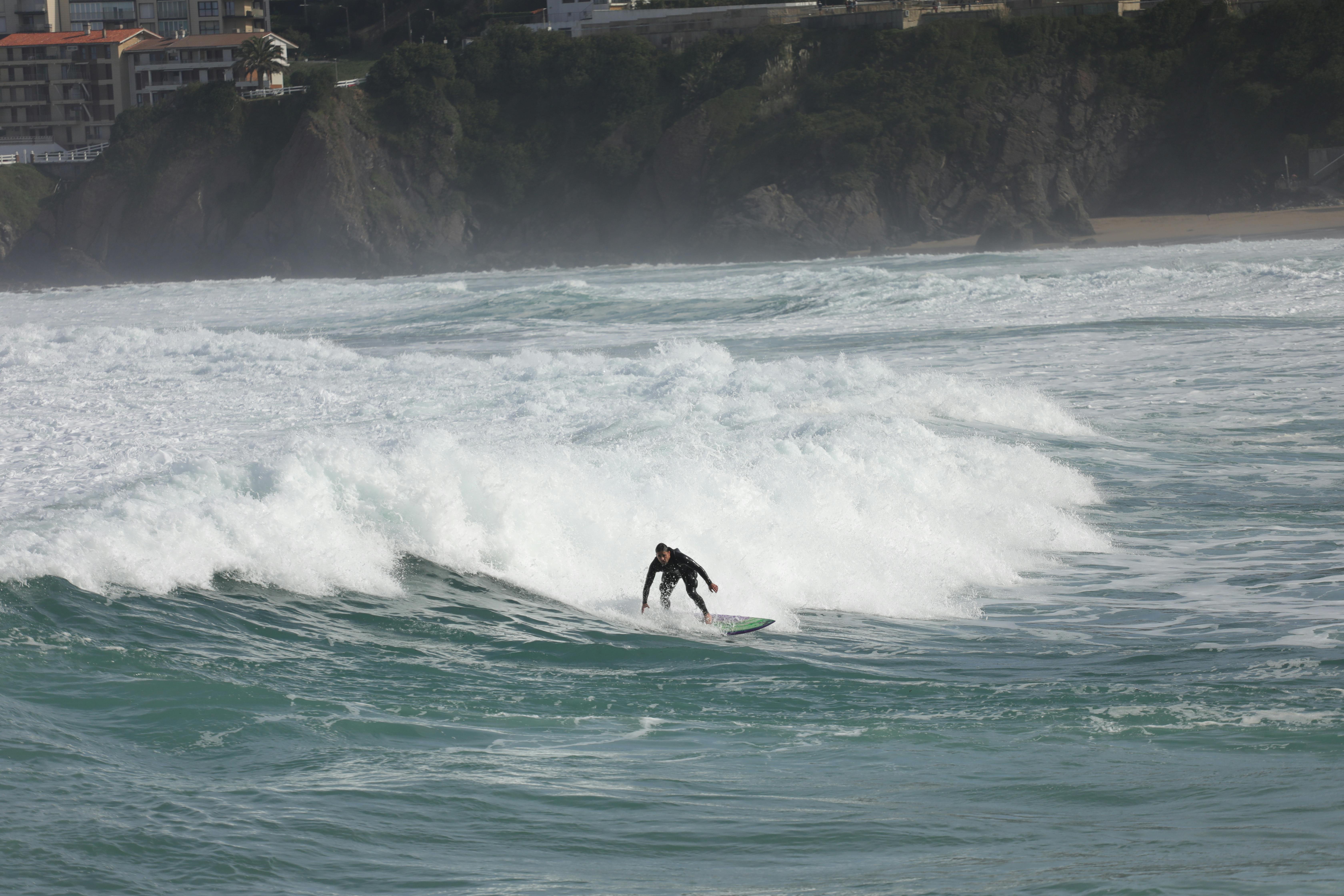 A surfer skillfully rides a wave on Bakio Beach, surrounded by dramatic coastal scenery in Bizkaia, Spain.