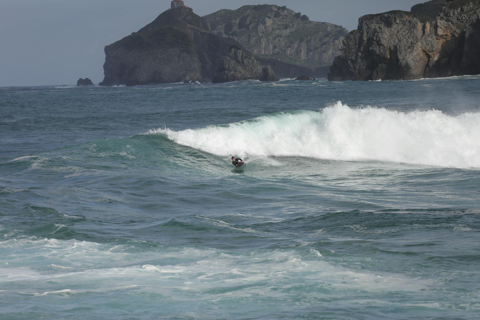 Budget-Friendly Adventures: Uncover The Most Affordable Ways To Explore The World 1 surfer gracefully rides a wave near rugged cliffs under a clear sky, embodying a dynamic surfing adventure.