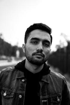 一张黑白肖像，画中是一位留着胡须、身穿户外牛仔夹克的年轻人