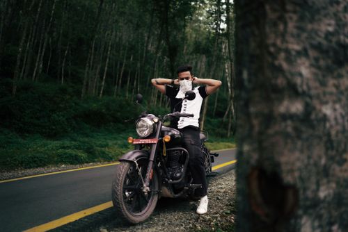 Free A man pauses with his motorcycle on a quiet forest road, offering a sense of adventure and freedom. Stock Photo