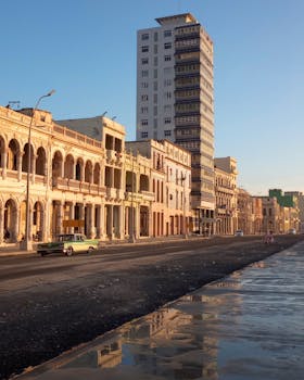 A classic car drives past historical buildings in La Habana, Cuba, under a warm sunset glow.