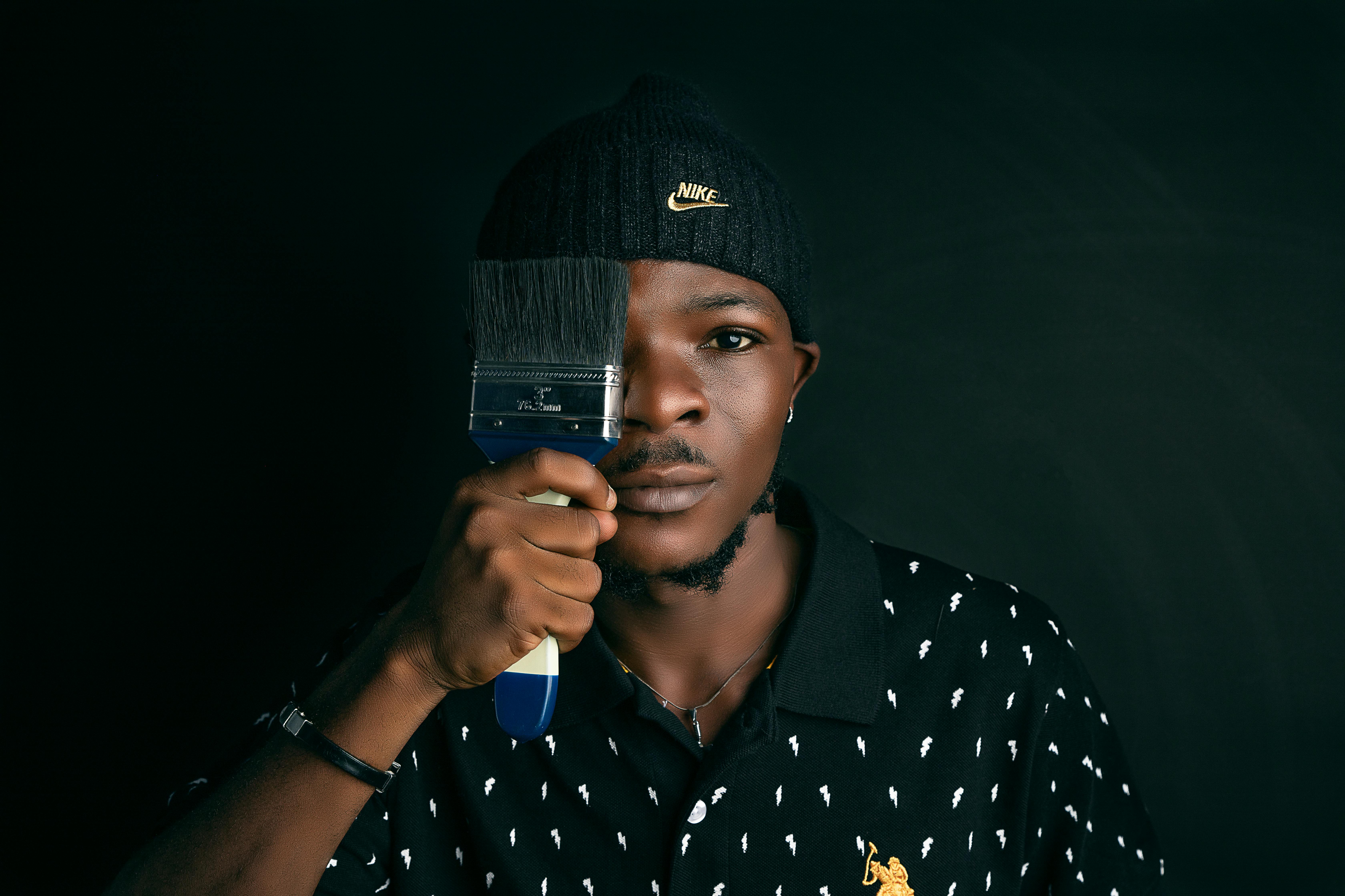 Creative portrait of a man holding a paintbrush against a dark background.