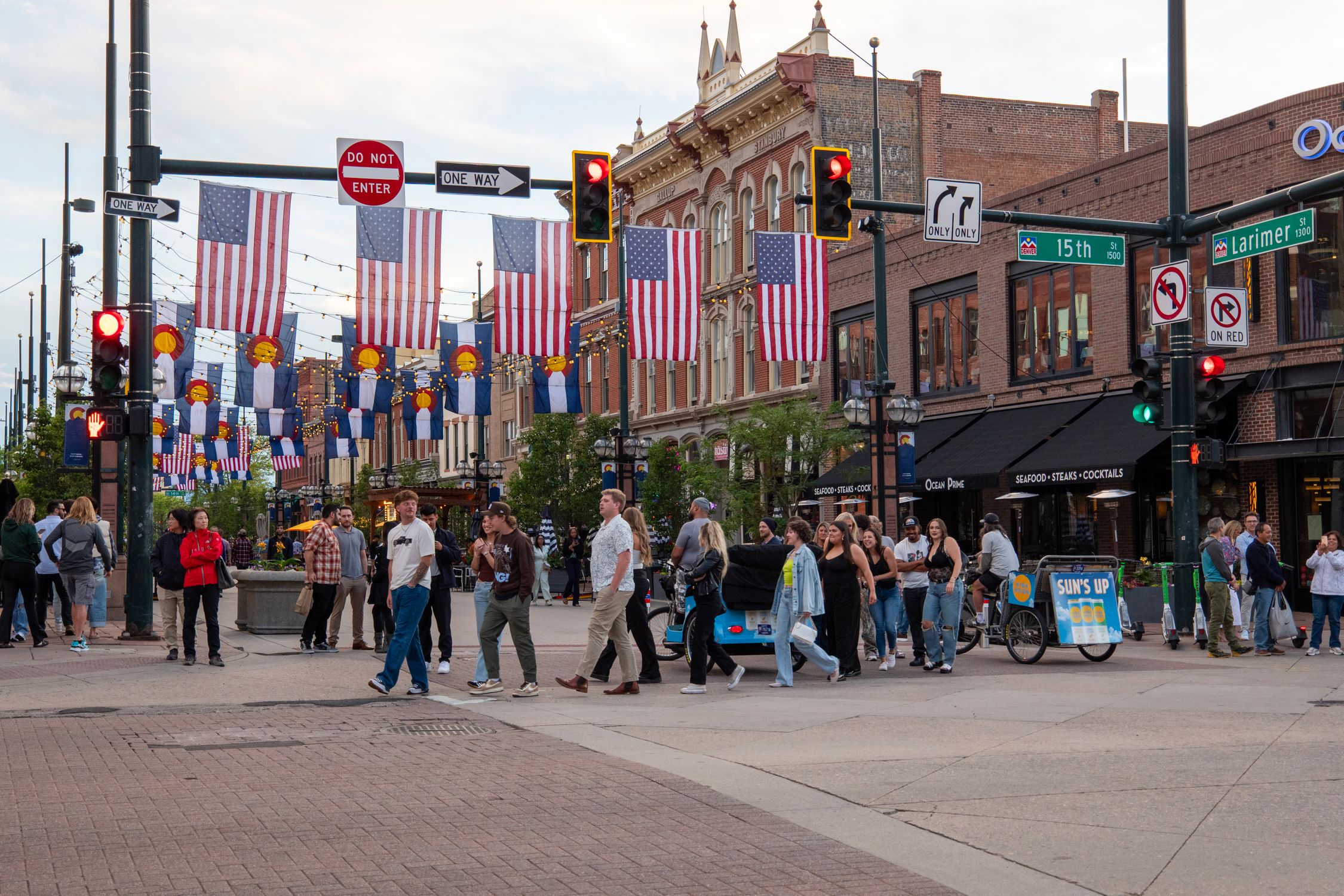 People crossing a lively intersection adorned with flags in downtown Denver.