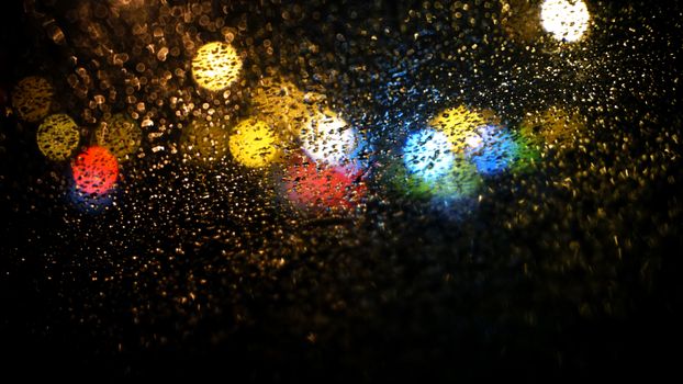 这张夜间玻璃上的抽象图像中，彩色雨滴与散景灯光交织，形成充满活力的纹理