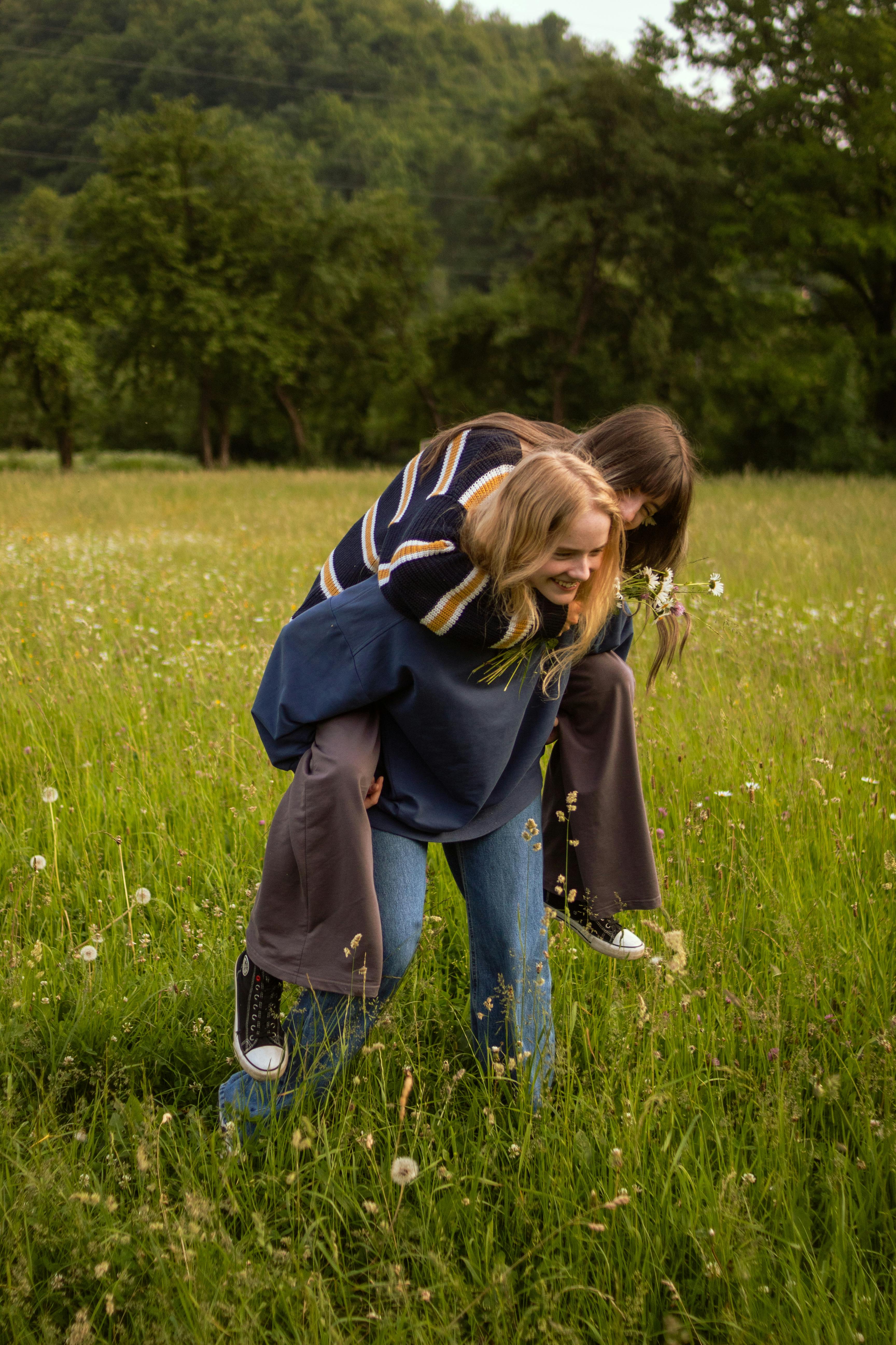 Two friends enjoying a piggyback ride in a vibrant green meadow filled with wildflowers.