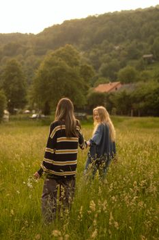 Two friends walk through a lush green meadow in summer's warm glow.
