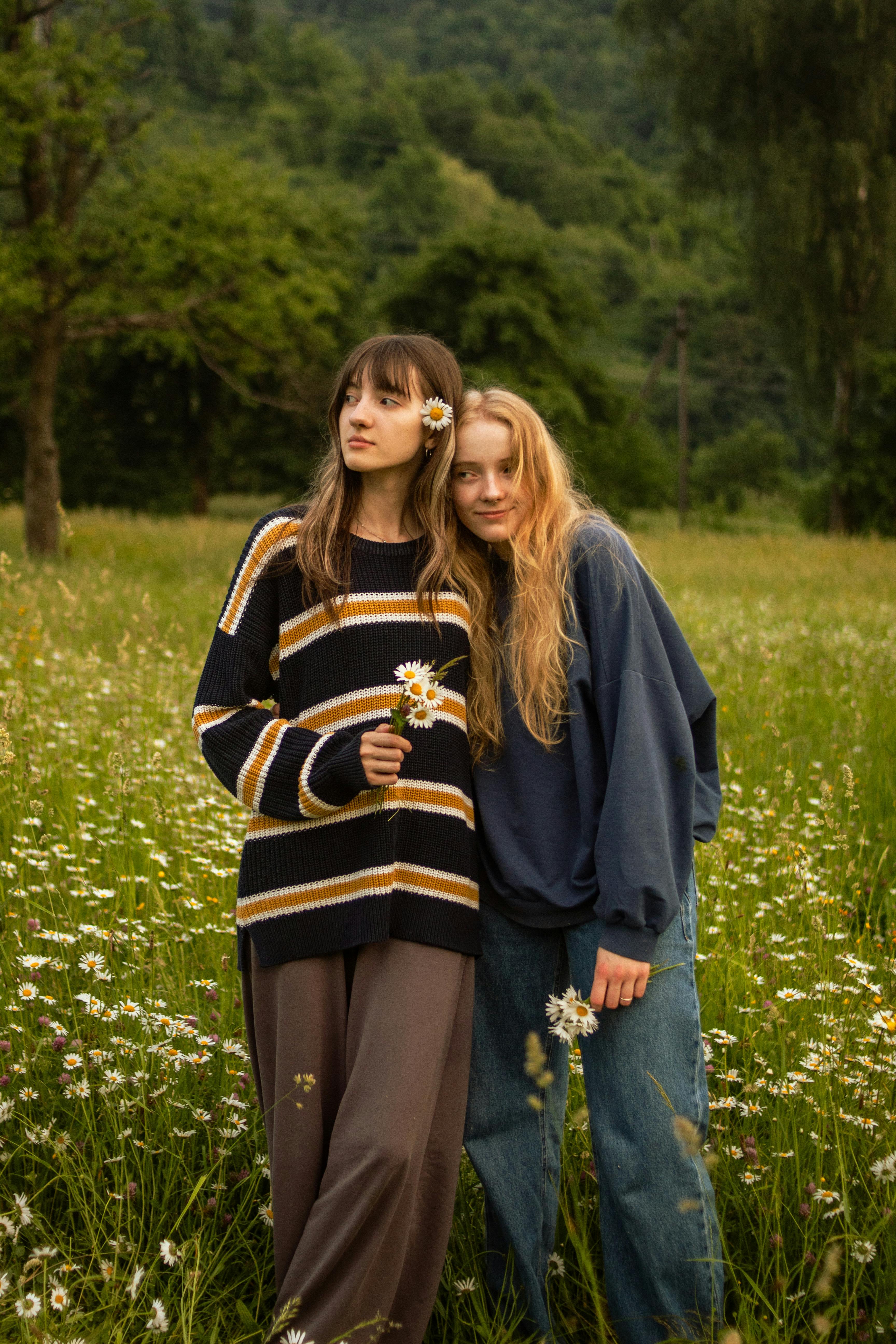 Two young women standing in a daisy field, enjoying a peaceful summer day.