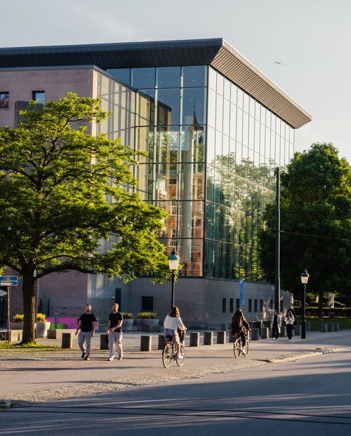 Free A contemporary glass building with cyclists passing by in Malmö, Sweden, on a sunny day. Stock Photo