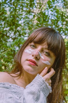 夏日晴天，一位脸上涂着白色云彩的无情少女站在树旁看着镜头