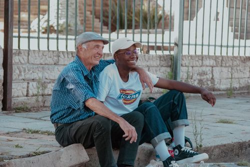 Free Two friends, an elder and a young adult, enjoying a sunny day sitting together outdoors in South Africa. Stock Photo