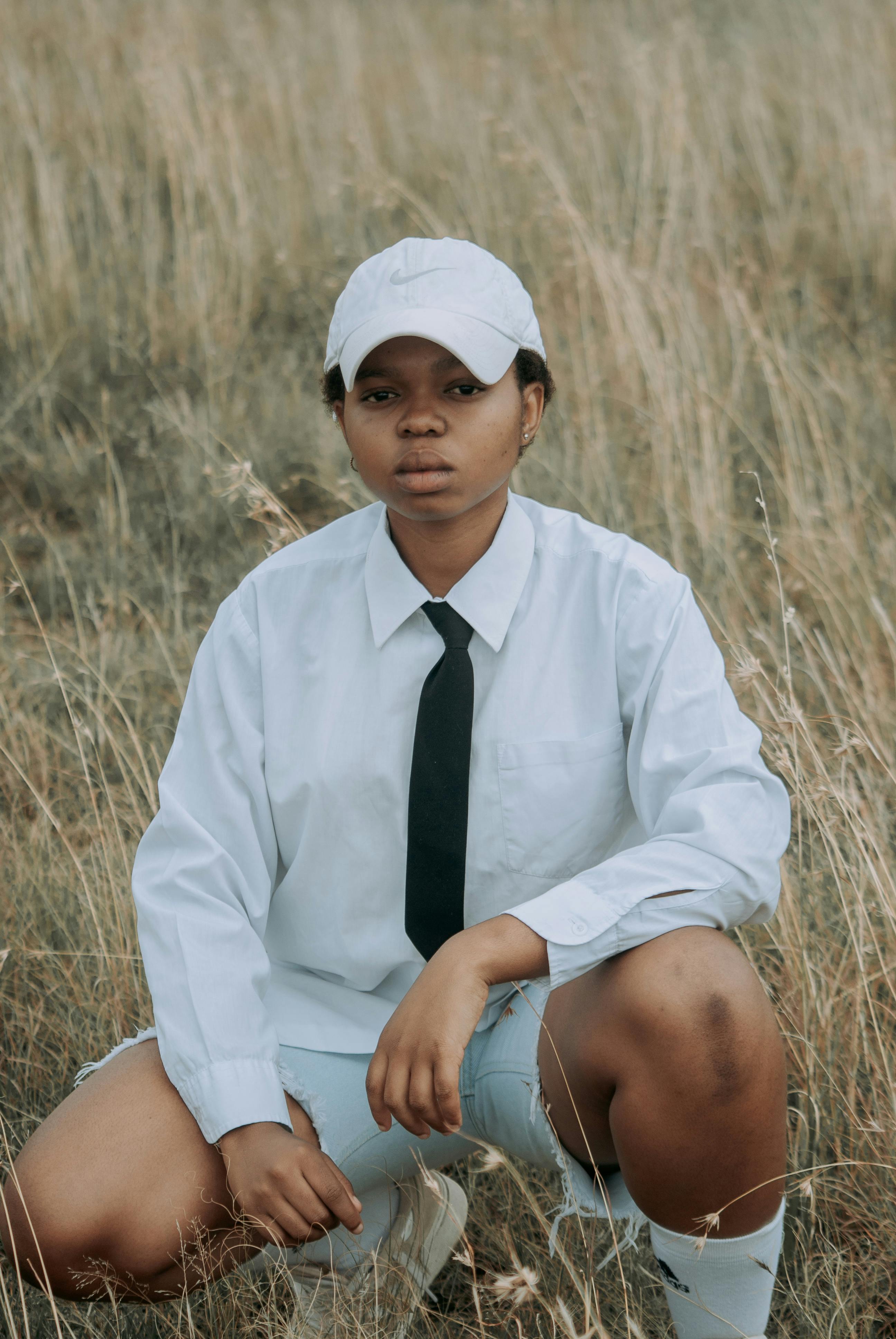 A young person in casual business attire sits in a grassy field, featuring a relaxed outdoor setting.