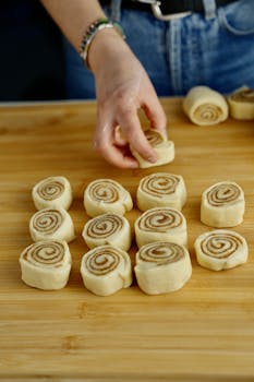 Hand arranging homemade cinnamon rolls, ready for baking, on a wooden board.