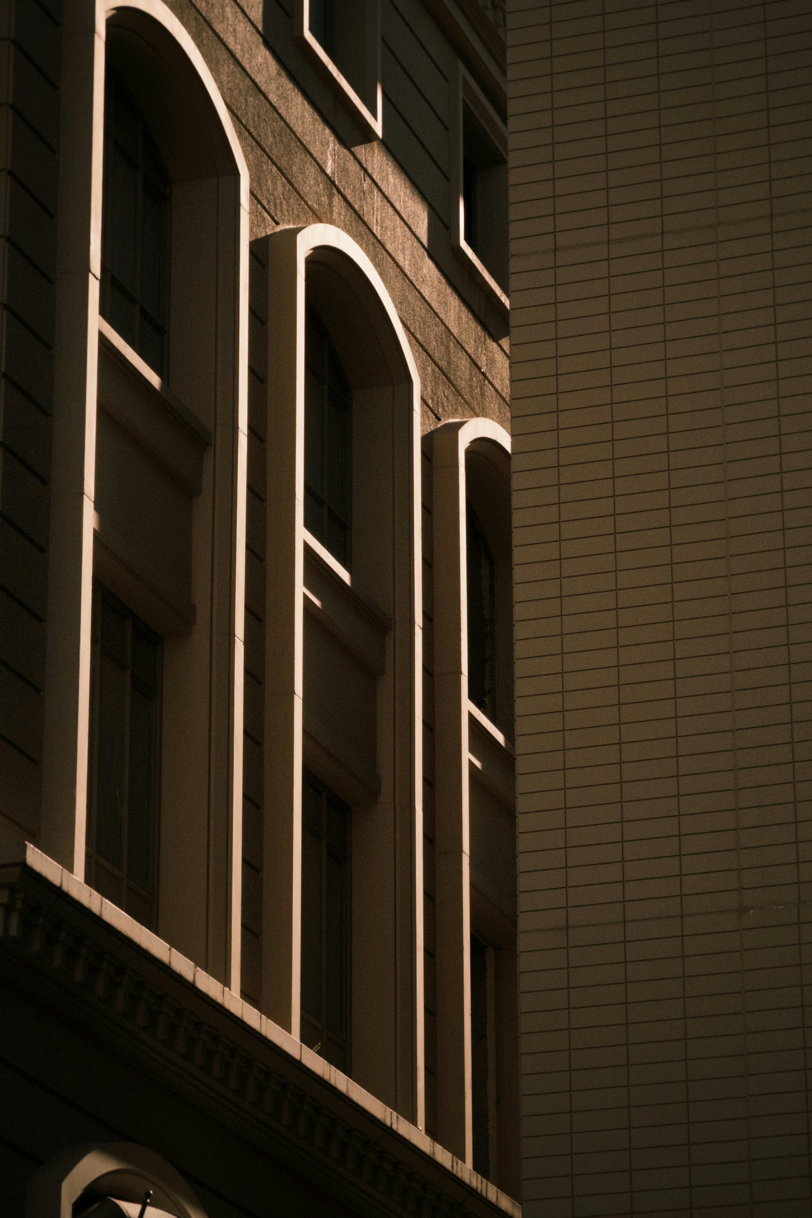 Free Close-up of a building facade with arches and sunlight creating dramatic shadows. Stock Photo