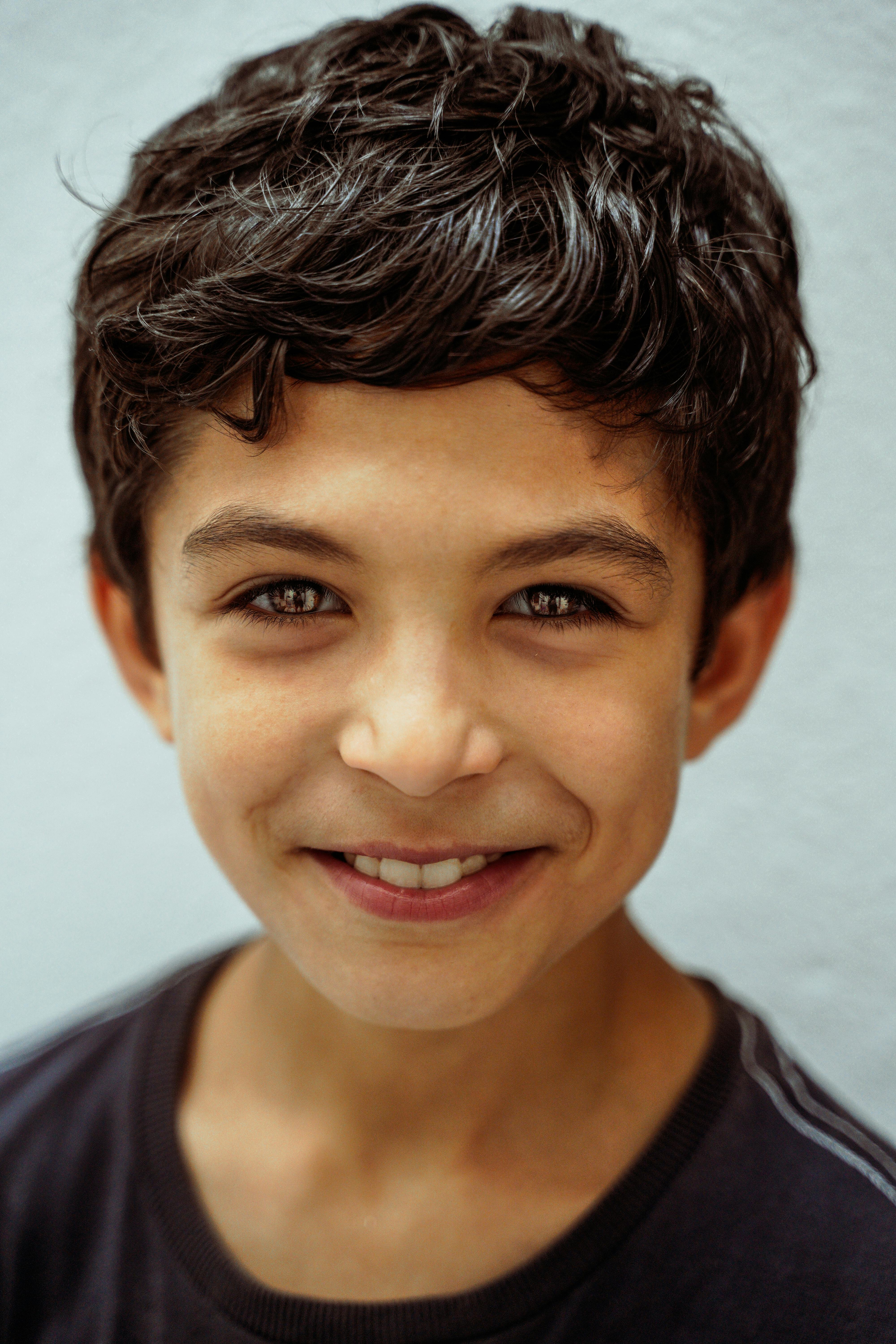 Close-up portrait of a young boy smiling warmly against a light blue background.