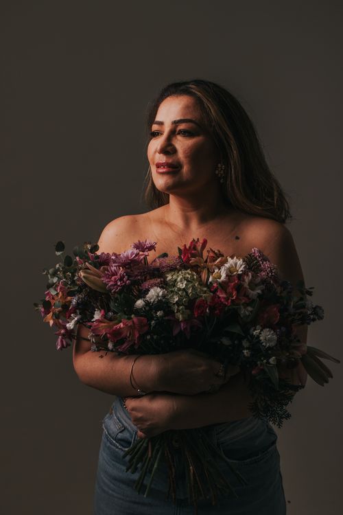 Free Portrait of a woman holding vibrant bouquets of flowers against a dark background, exuding elegance and serenity. Stock Photo