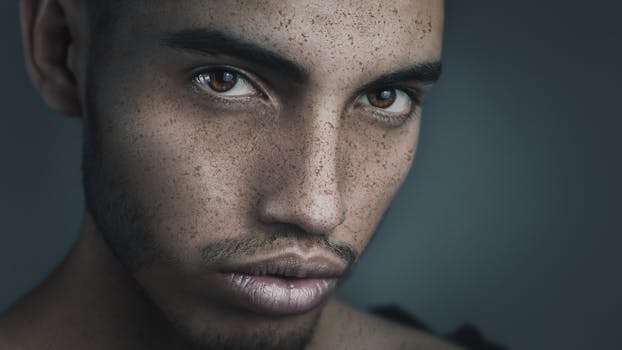 Close-up portrait highlighting the intense gaze of a freckled man with dark eyes, captured in a soft, muted setting.