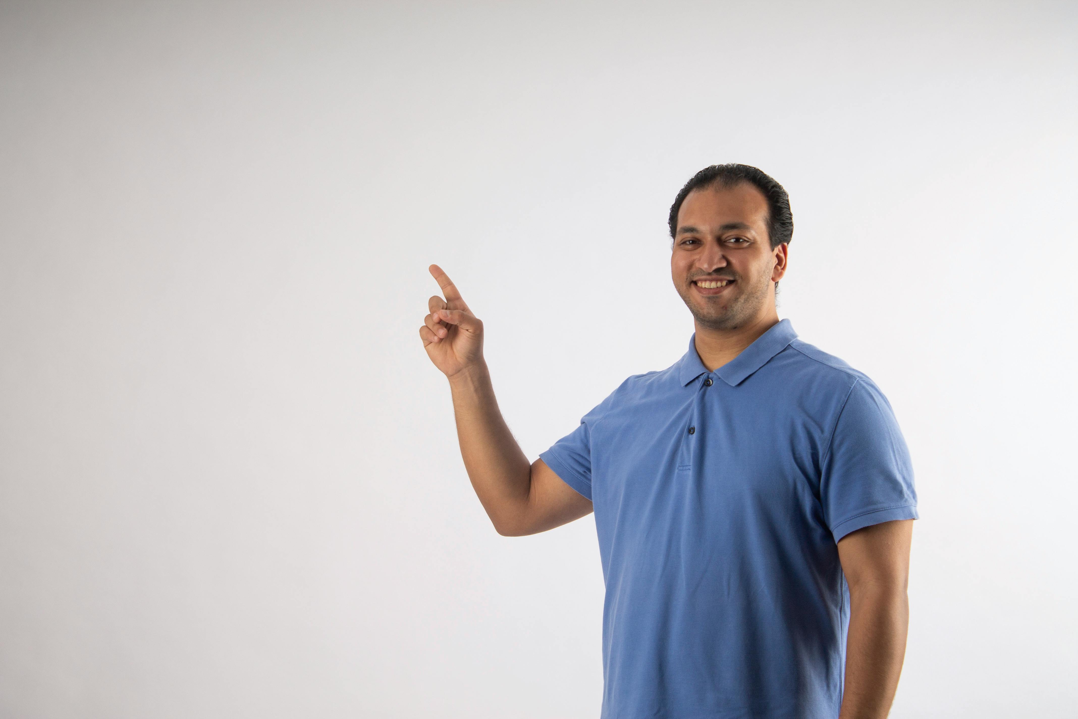 De franc Home alegre amb polo blau assenyalant cap amunt contra un fons llis, suggerint una direcció o una idea. Foto d'estoc