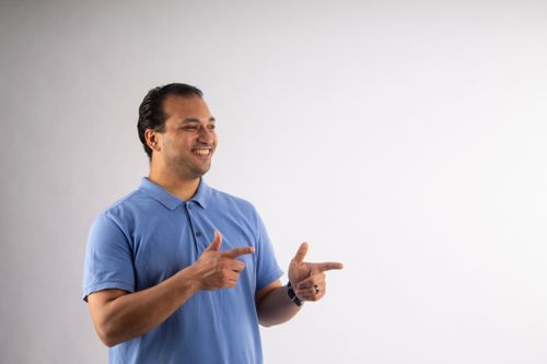 Free Cheerful man in a blue shirt making finger guns gesture on a white background. Stock Photo