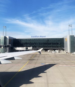 View of Frankfurt Airport terminal with airplane wing, clear blue sky, and runway.