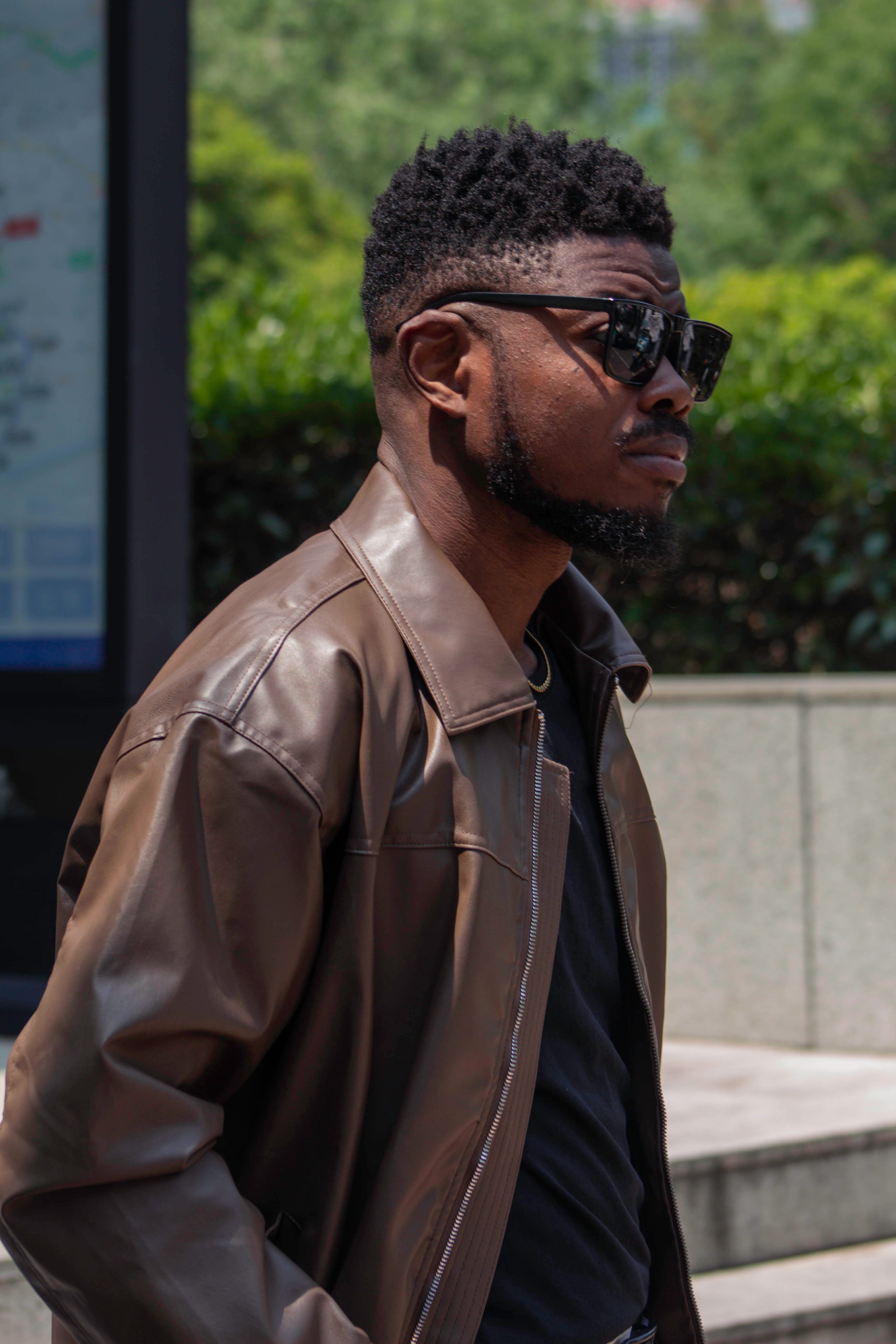 Confident man wearing sunglasses and leather jacket in an urban setting, depicting modern fashion.