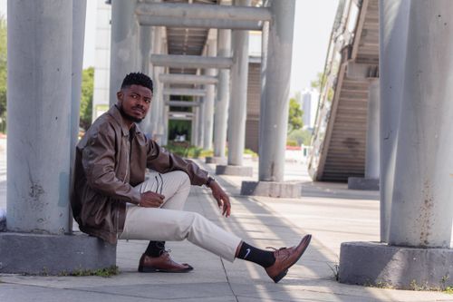 Free Stylish man in casual attire sitting under modern architecture outdoors. Stock Photo