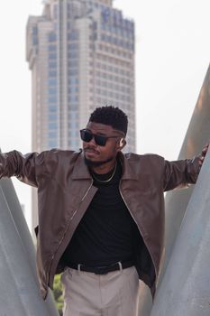 Stylish man in leather jacket and sunglasses posing against a skyscraper backdrop.