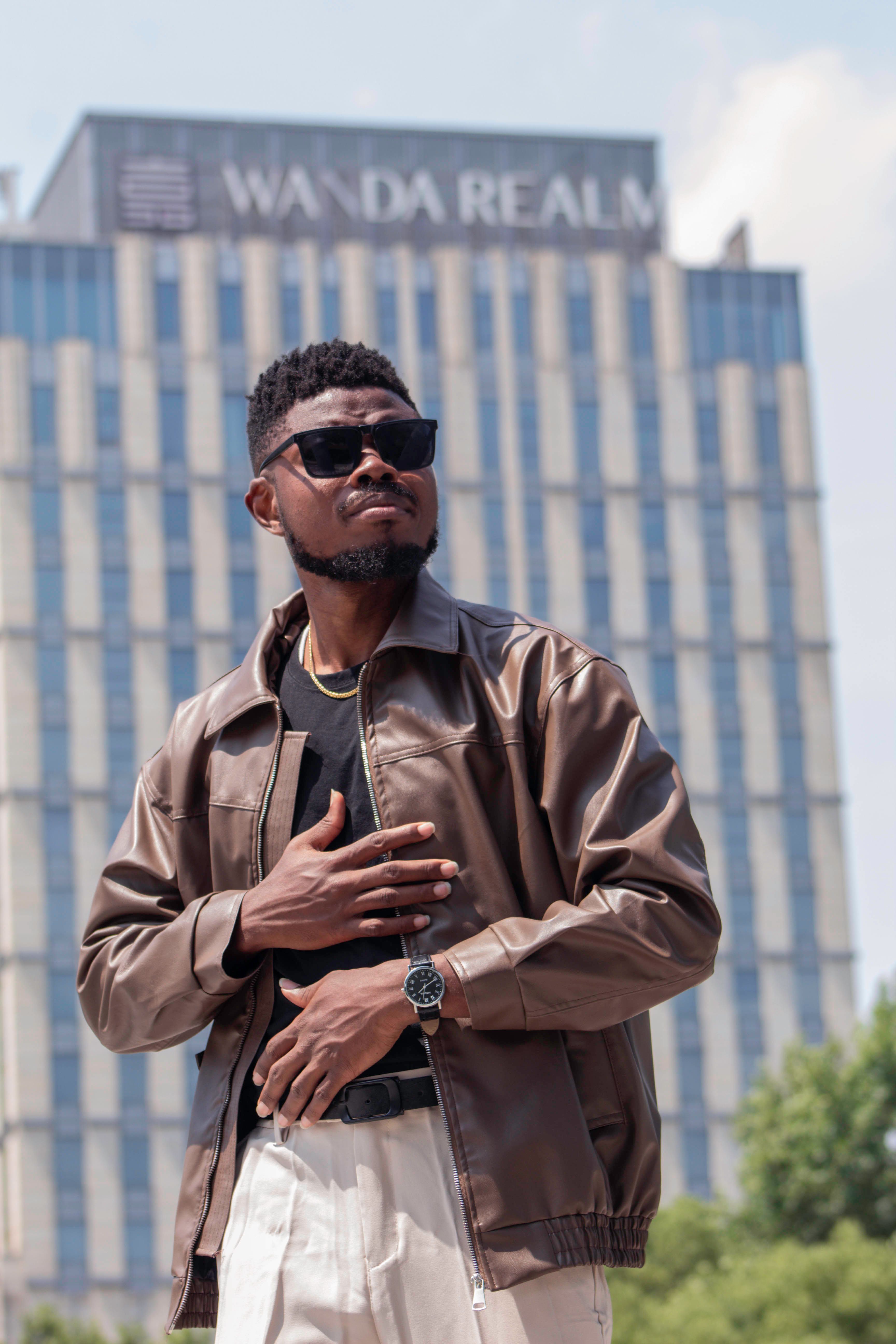 Stylish individual in casual attire posing confidently outdoors with a skyscraper background.