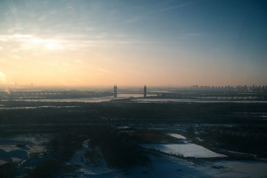 Aerial sunset view of city skyline with bridge and snowy landscape, capturing serene winter beauty.