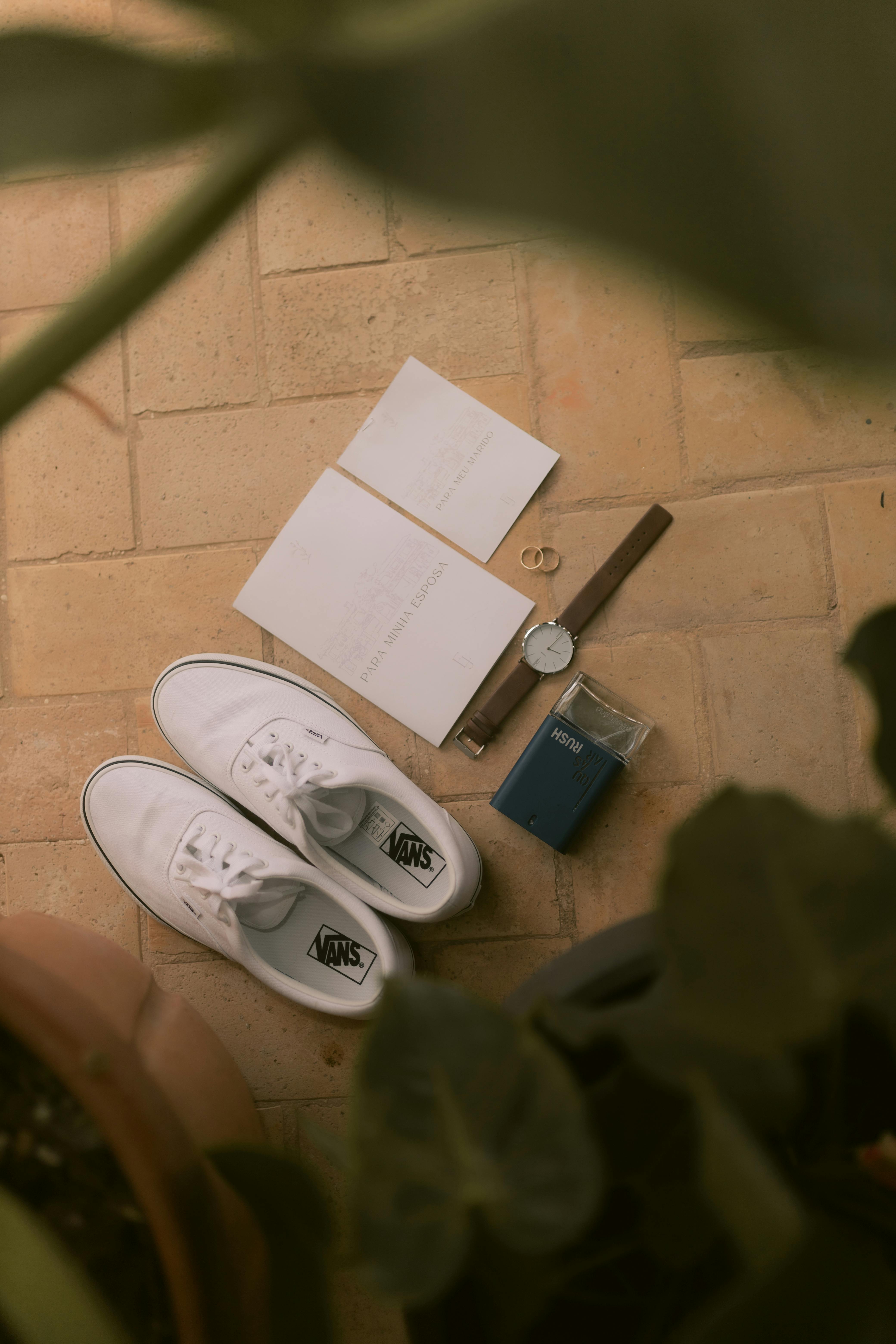 免費 美觀的平面佈置，瓷磚表面上擺放著白色運動鞋、手錶、記事本和香水。 圖庫相片