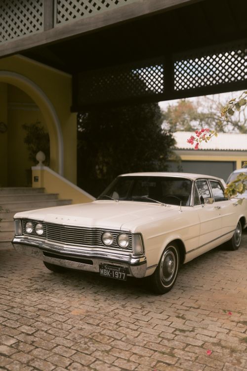 Free Classic vintage white car parked on cobblestone driveway in front of a yellow house, creating a nostalgic vibe. Stock Photo