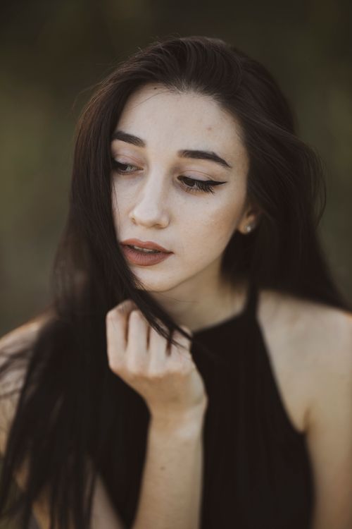 Free Close-up portrait of a young woman with long dark hair and elegant makeup, gazing pensively outdoors. Stock Photo