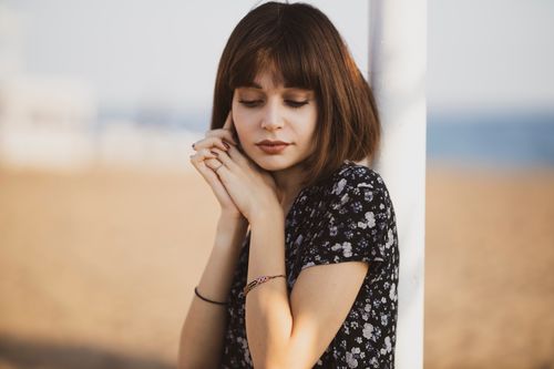 Free A serene woman in a floral dress posing thoughtfully at the beach during sunset. Stock Photo