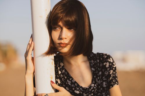 Free Portrait of a young woman leaning on a pole under the warm sunlight. Stock Photo