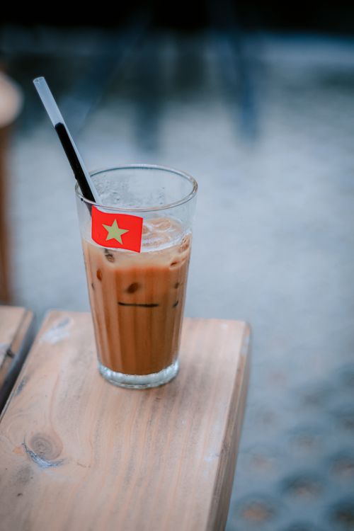 Free Glass of iced Vietnamese coffee with a flag stirrer on a wooden table, outdoors. Stock Photo